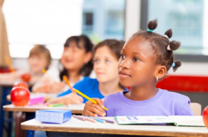 Young girl sitting at school desk, listening attentively